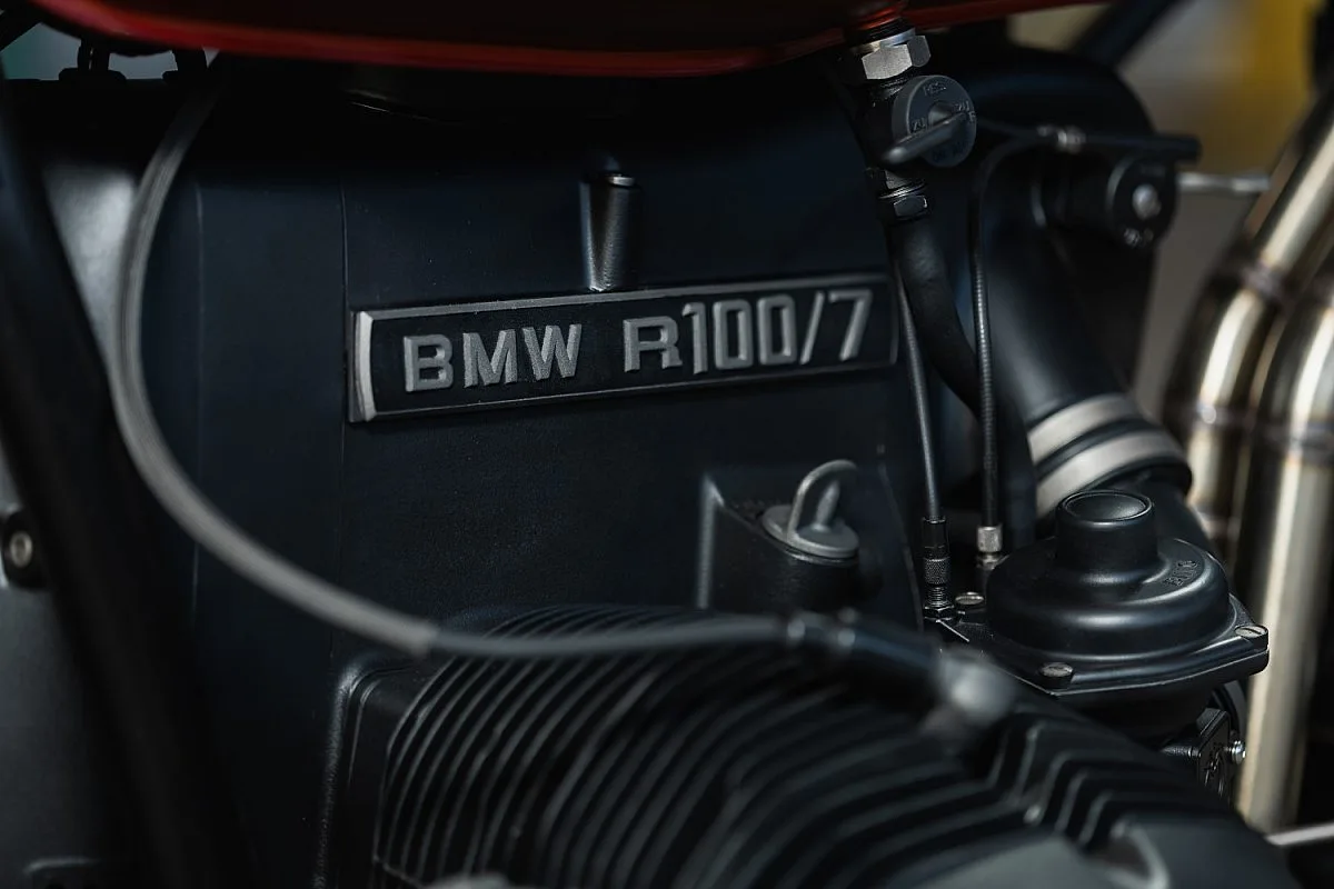 Placa «BMW R100/7» del motor bóxer negro mate, con cables trenzados y colectores de acero inoxidable al fondo