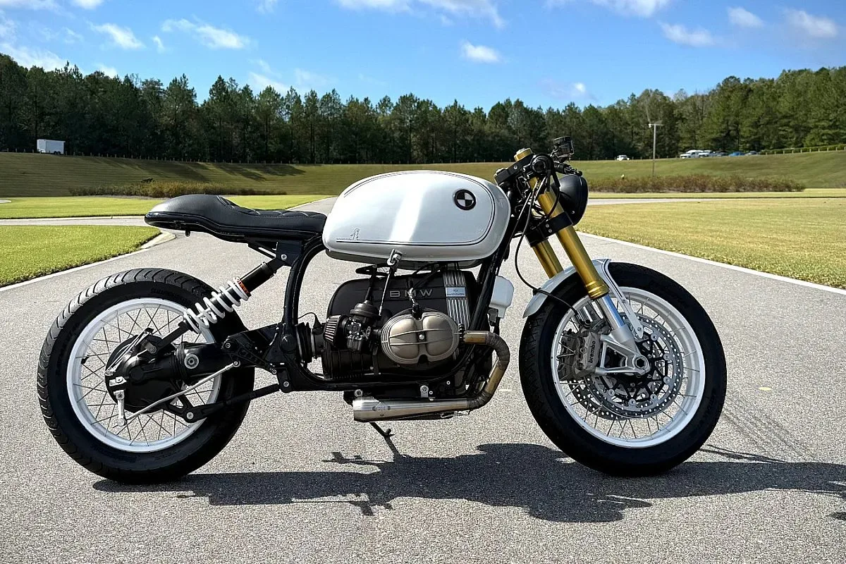 BMW R100 cafe racer de Marekswerk de perfil: depósito blanco, asiento negro capitoné, horquilla invertida dorada, llantas blancas y escape de acero inoxidable