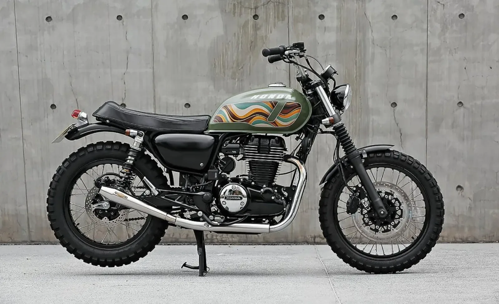 Honda CB350 scrambler de Mark Motorcycles vista de perfil: depósito verde militar con decoración ondulada de los setenta, asiento negro, ruedas de radios con neumáticos de tacos y escape cromado