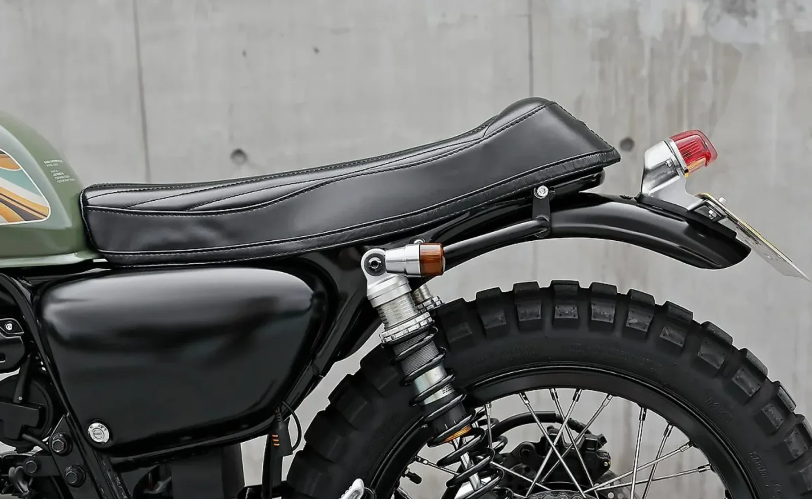 Detalle del asiento negro con costuras, el guardabarros trasero, el piloto de estilo Lucas, un intermitente ámbar y el amortiguador de la Honda CB350 preparada