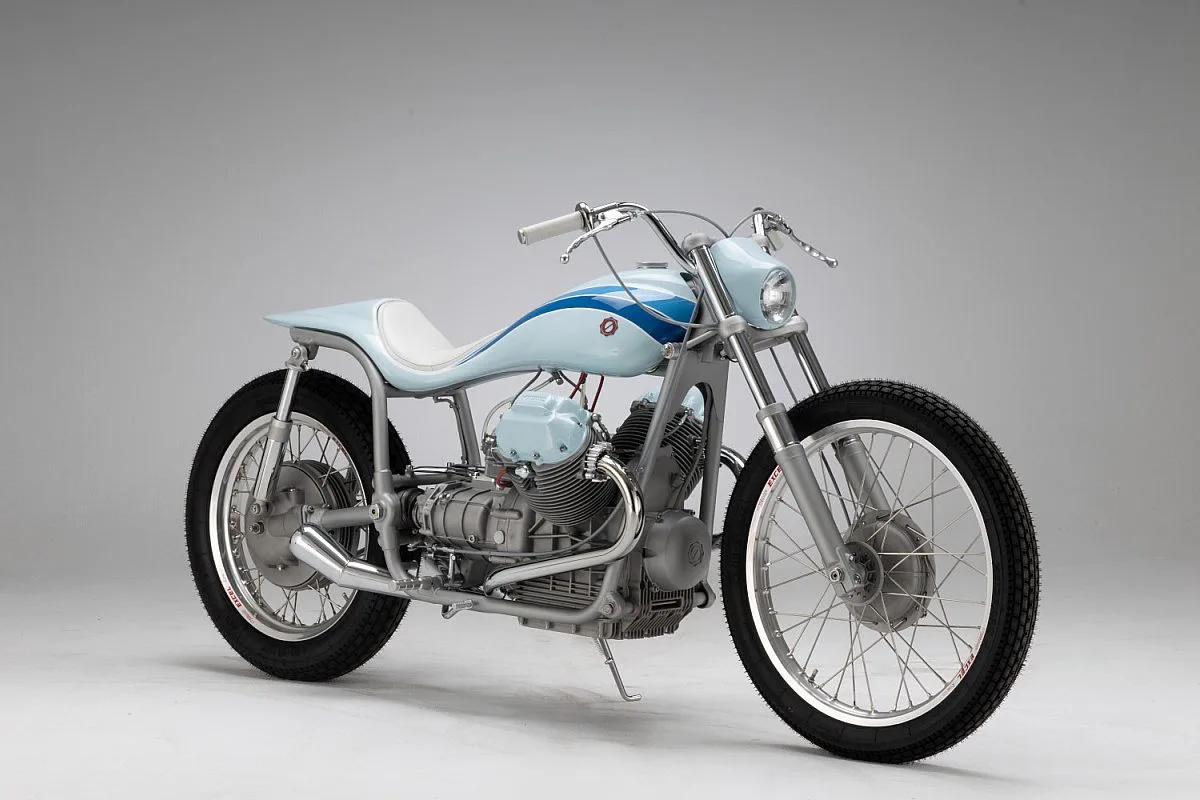 Moto Guzzi V7 «Bonanza» en tres cuartos delanteros: carrocería azul claro con franjas azules, asiento blanco y bastidor al descubierto