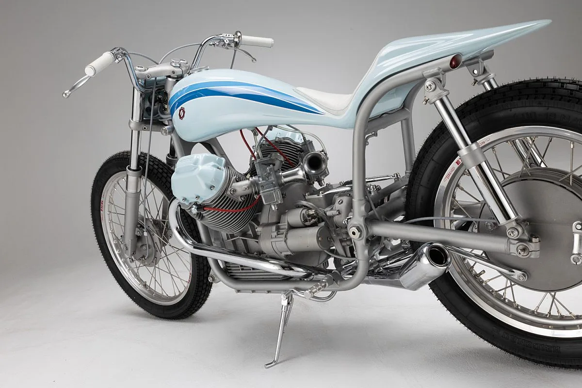 Detalle del lado izquierdo de la Moto Guzzi V7 «Bonanza»: cilindro con tapa azul, carburadores, escape cromado y subchasis tubular