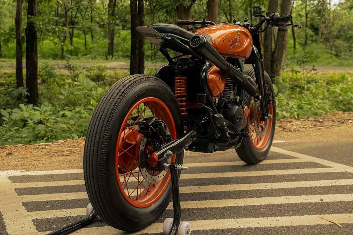 Vista trasera tres cuartos del tracker de Garuda Machina: escape negro, monoamortiguador naranja y neumático Shinko de dibujo clásico