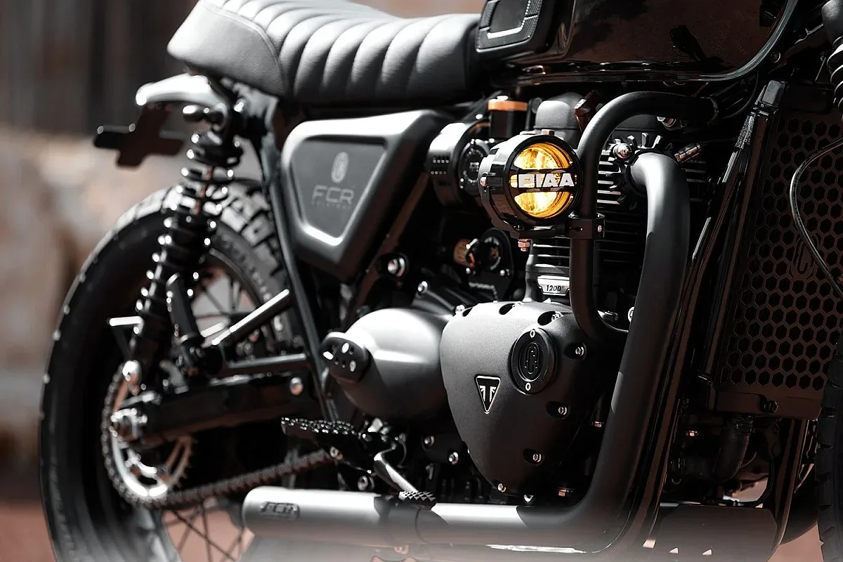 Foco auxiliar amarillo PIAA en la defensa del motor de la Triumph T120 de FCR Original, junto al escape negro y la tapa de motor con el logotipo Triumph
